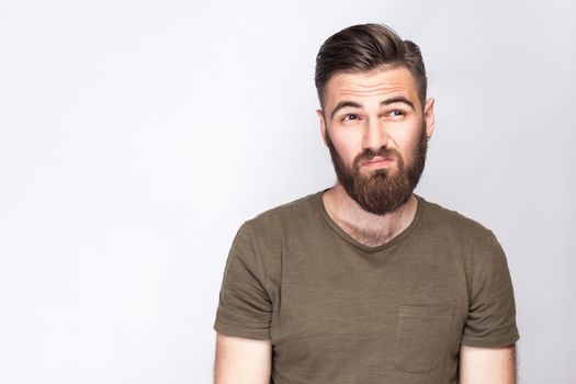 Portrait of thoughtful bearded man with dark green t shirt against light gray background. studio shot. .