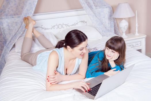 Happy mother and daughter do online shopping and pay with credit card with laptop lying on bed in bedroom. Happy family. Studio shot.