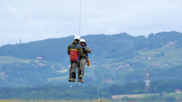 Cerklje ob Krki Slovenia MAY 29, 2022 Air rescuers dropped from a hovering helicopter to rescue people in emergency in the rain. Bell 412 of Slovenian Air Force. Copy Space