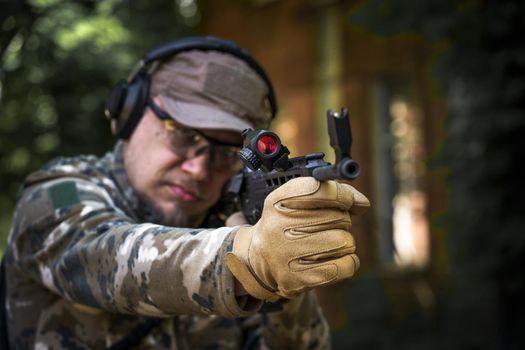 Shooter with a gun in military uniform tactical hearing protector headset. Police training in shooting gallery with weapon. Civil police man in tactical training course. Selective focus on hand.