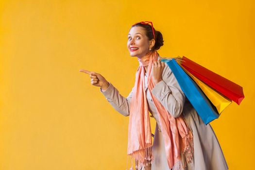 Happiness young adult woman pointing finger on copy space and looking at camera and toothy smile. On yellow background. Isolated shot