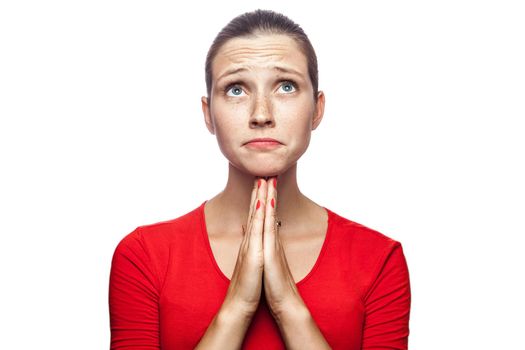 Portrait of unhappy pleasing woman in red t-shirt with freckles. looking up and wishing, studio shot. isolated on white background.