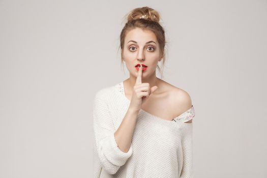 Secrecy sign. Blone woman with big eyes, showing secret shh sign. Studio shot, isolated on gray background
