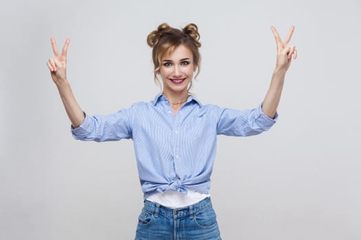 Young beautiful blonde woman with blue dress and head band showing peace sign. Isolated studio shot on gray background.