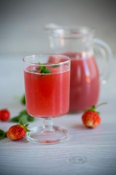 Cold summer strawberry kvass with mint in a glass on a wooden light table