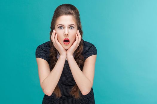 Amazement woman looking at camera with touching cheeks. Indoor, studio shot on blue background