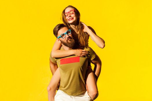 Piggyback. Happiness friend looking at camera and posing on yellow background. Studio shot