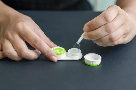 Girl takes contact lens out of container with tweezers. Black background, close-up, side view