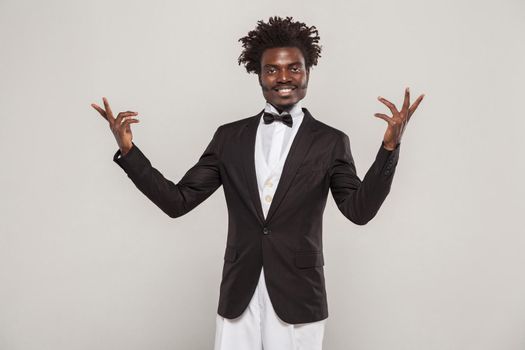 African well dressed singer or actor with afro hair style in classic style tuxedo and bow tie toothy smiling. Indoor, isolated studio shot on gray background