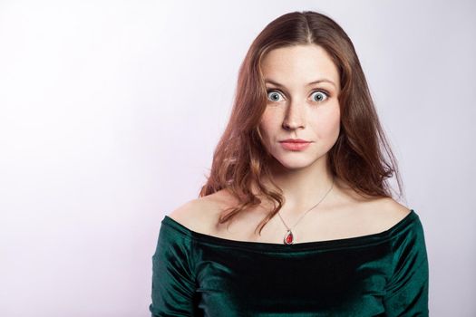 Portrait of surprised woman with freckles and classic green dress. studio shot on silver gray background.
