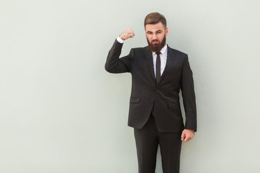 Strong, seriously bearded businessman showing muscle and looking at camera. Indoor shot, gray background