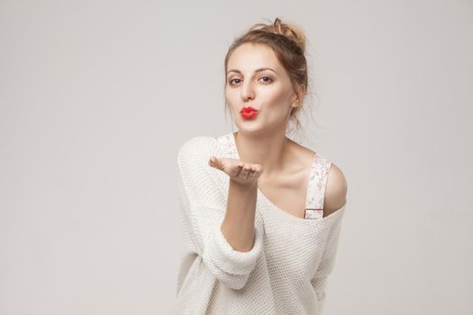 Romantic woman send air kiss at camera. Studio shot, isolated on gray background