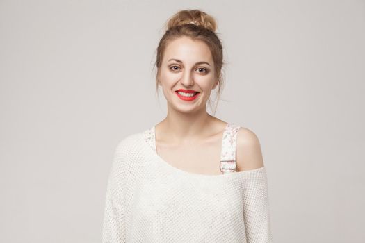 Happiness young blonde woman looking at camera and toothy smile. Studio shot, isolated on gray background