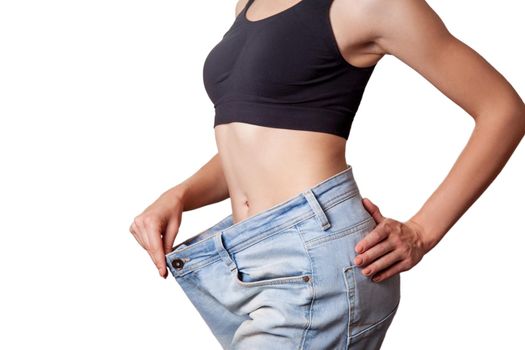 Close-up of slim waist of young woman in big jeans showing successful weight loss, isolated on white background, diet concept.