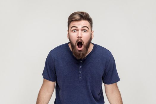 Unbelievable news! Young adult crazy man with opened mouth looking at camera. Studio shot, gray background