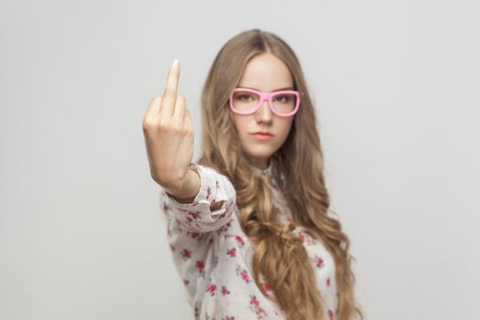 Unhappy woman, showing fuck sign at camera. Focus on hand. Indoor shot, gray background