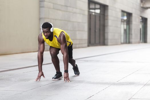 African man in running start pose on the city street. Outdoor shot, morning. Spring or summer