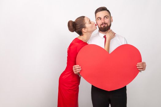 Man wish something, smiling, perfect woman kiss him at cheek. Indoor, studio shot, isolated on gray background