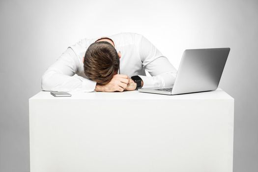 Sweet dreams tired in the work station. Portrait of sleepy tired freelancer in white shirt are sitting in office is snoozing at his work place near laptop. Indoor, studio, gray background, isolated