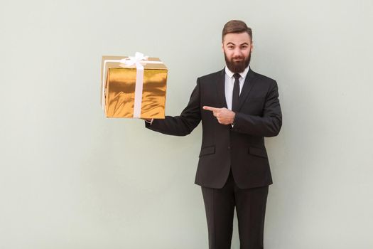 Handsome bearded businessman pointing finger gift box and happy looking at camera. Indoor shot, gray background