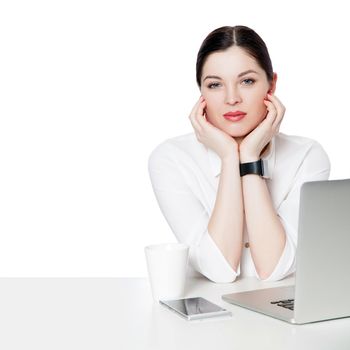 Portrait of calm attractive brunette businesswoman with makeup in white shirt sitting with laptop, touching her face and looking at camera with smile. indoor studio shot, isolated in white background.