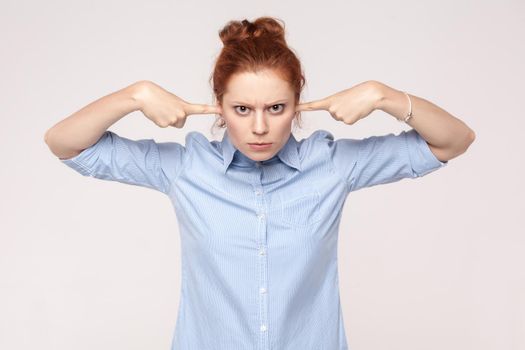 I do not want to hear from you! Aggressive ginger woman holding fingers on ears and looking at camera. Studio shot