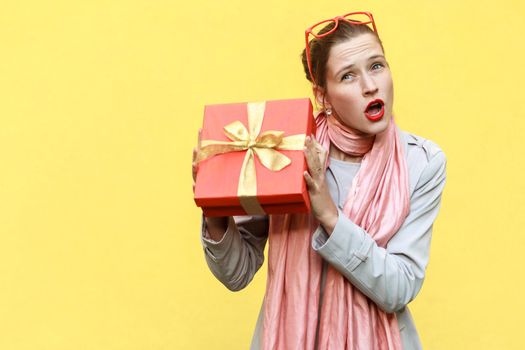 Cant stand, Its my! Playfully young adult girl holding gift box. Isolated on yellow background, studio shot