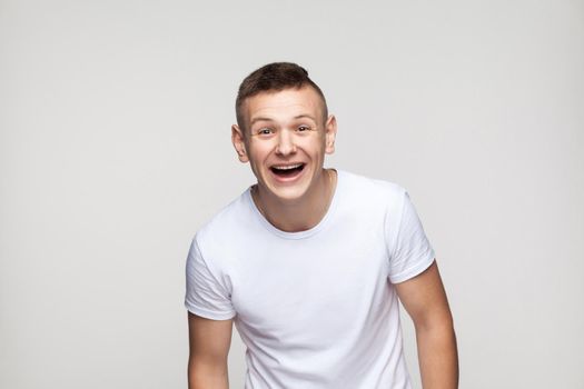 Young success man looking at camera and toothy smile. Studio shot, gray background