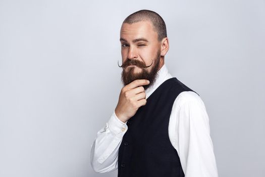 thoughtful, Handsome businessman with beard and handlebar mustache looking at camera and thinking. studio shot, on gray background.