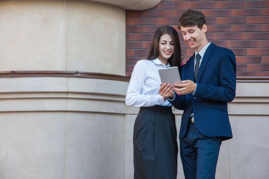 Business people using a digital tablet outdoor. Businessman and Businesswoman standing friendly on steps and using tablet with smile in the city.