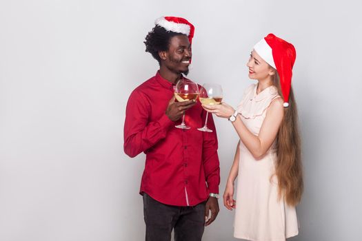 Flirt and love concept. Man and young adult woman in christmas cap, holding glasses with champagne and looking each other with love. Indoor shot