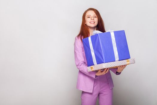 Happy birthday! Red haired cute girl holding her gifts and have a happy look. Studio shot