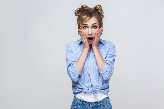 Human face expressions and emotions. Blonde woman screaming with shock, holding hands on her cheeks. Isolated studio shot on gray background.