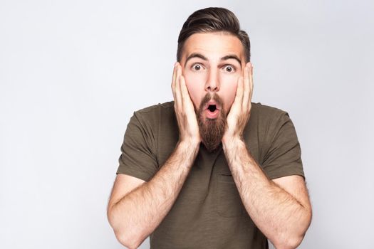 Portrait of surprised bearded man with dark green t shirt against light gray background. studio shot. .