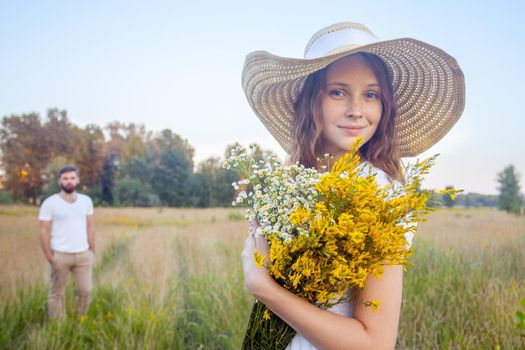 Beautiful woman holding bouquet of yellow flowers and looking at camera with her boyfriend on background.