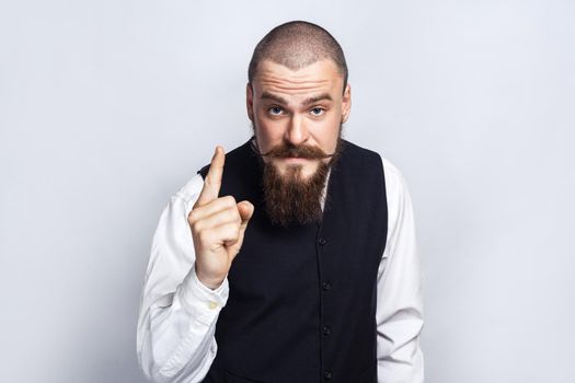 Warning. Handsome businessman with beard and handlebar mustache looking at camera with serious face and finger warning. studio shot, on gray background.