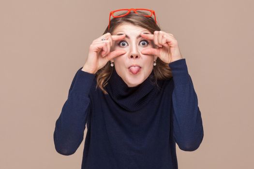 Crazy woman looking at camera and tongue out. Studio shot, light brown background