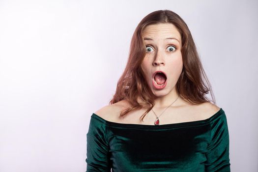 Portrait of shocked woman with freckles and classic green dress. studio shot on silver gray background.