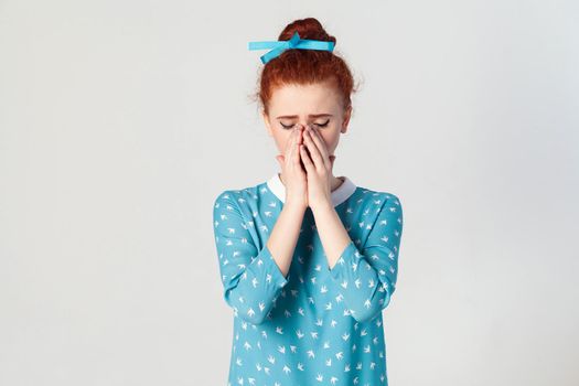Portrait of unhappy, depressed and crying young caucasian girl with ginger hair feeling ashamed or sick, covering face with both hands, keeping eyes closed.