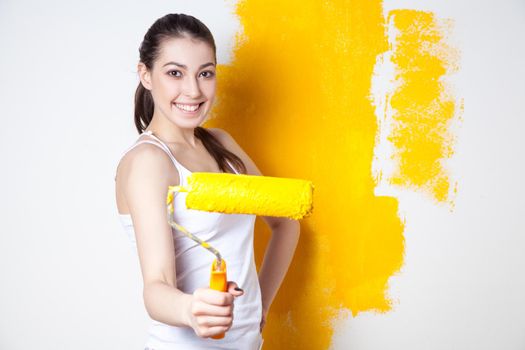 Beautiful young caucasian model in coloured shorts and white shirt and posing holding outrigger in her hands, painting the wall and looking at camera. Studio shot.