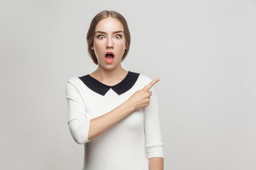 Boss pointing finger at copy space, and looking at camera with shocked face and big eyes. Studio shot, gray background