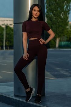 Portrait of a fitness girl in fashionable sportswear on the background of a commercial building. Lifestyle, culture of a well-groomed female body.