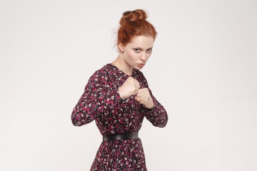 Ready to fight! Aggressive redhead women with bun hair looking at camera with seriously face. Indoor, isolated on gray background