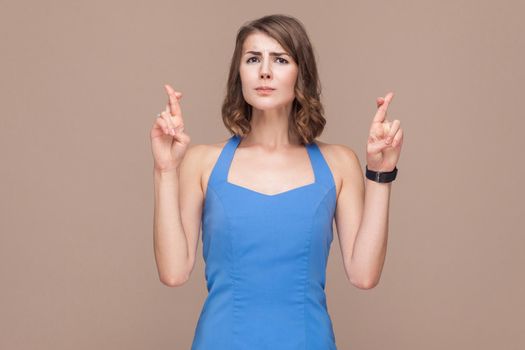 Hope, wish concept. Well dressed woman crossed fingers and looking at camera. Studio shot