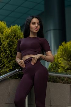 Portrait of a fitness girl in fashionable sportswear on the background of a shopping center building. Lifestyle, culture of a well-groomed female body.