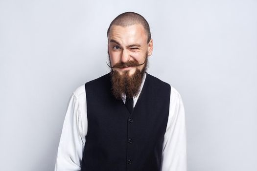 Wink. Handsome businessman with beard and handlebar mustache looking at camera and winking. studio shot, on gray background.