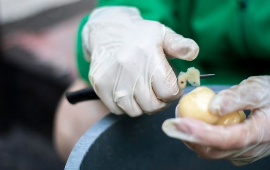 Woman's hands in white gloves peel raw new potatoes, close-up. Cleaning organic potatoes. Detail of female hands peeling fresh yellow potato with kitchen knife, food preparation concept