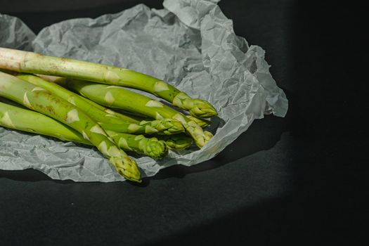 fresh green asparagus lies on a white parchment on a dark gray background. proper nutrition. Lifestyle. place for text