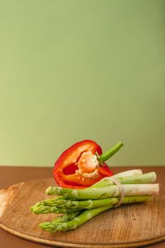Vegetables lie on a wooden board: tomatoes, asparagus, cucumbers, red bell peppers. brown, light green background. place for text