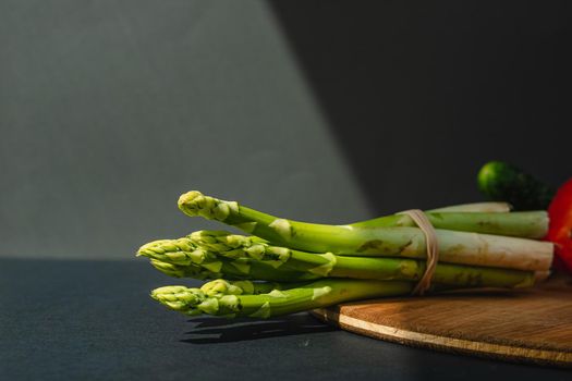 branches of fresh green asparagus on a wooden board, dark gray background, top view. Basic trend concept with copy space